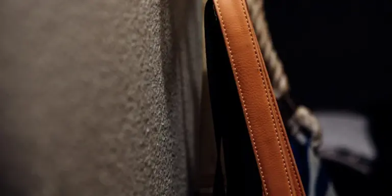 Close-up of a brown leather bag strap with visible stitching, showing leather texture.