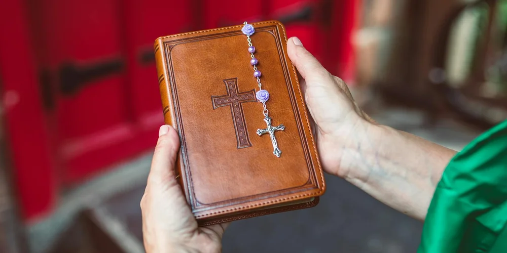 Close-up of a brown leather-bound book with a rosary draped over its cover, held by hands.