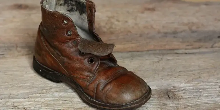 Brown, worn leather boot with scuffs on a wooden floor