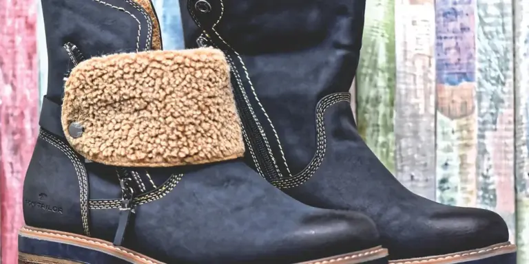 Close-up of black leather boots with tan shearling accents, against a colorful wooden background.