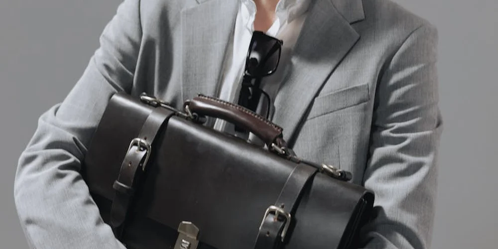 A person in a gray suit holds a black leather briefcase, illustrating premium leather care decisions.