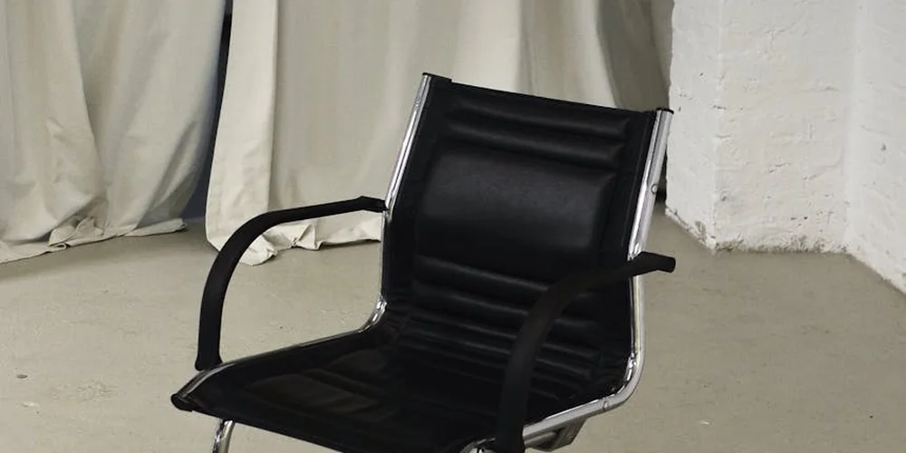 Black leather chair in a minimal studio with light curtains in the background