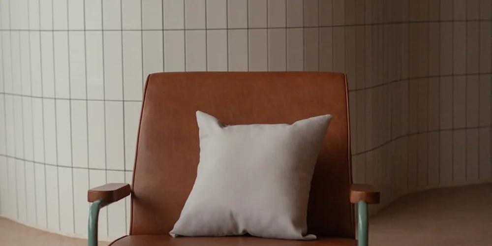 Brown leather armchair with a white cushion in a tiled room