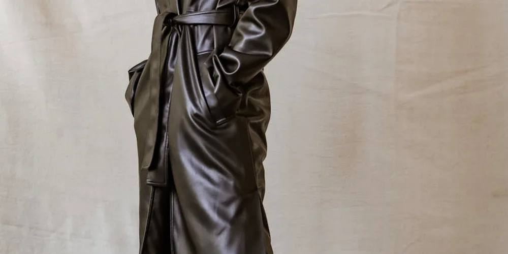 Close-up of a person wearing a dark, glossy leather coat with a tied belt.