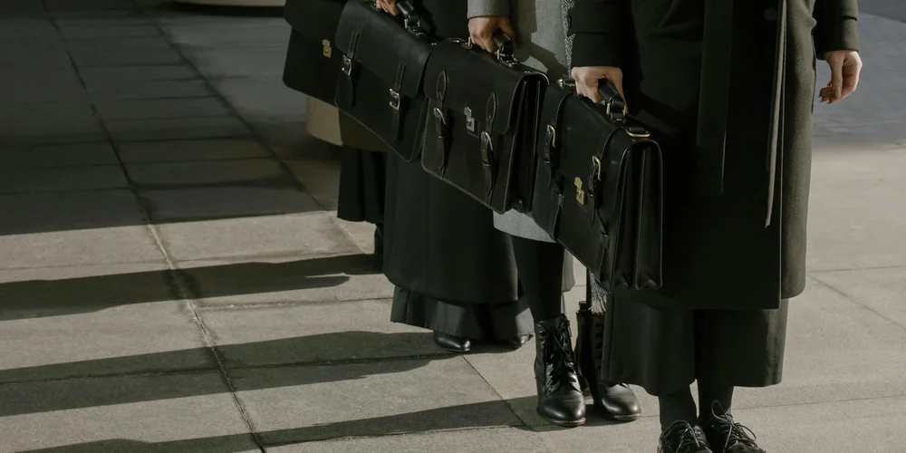 People walking on a city sidewalk, each carrying black leather briefcases and bags
