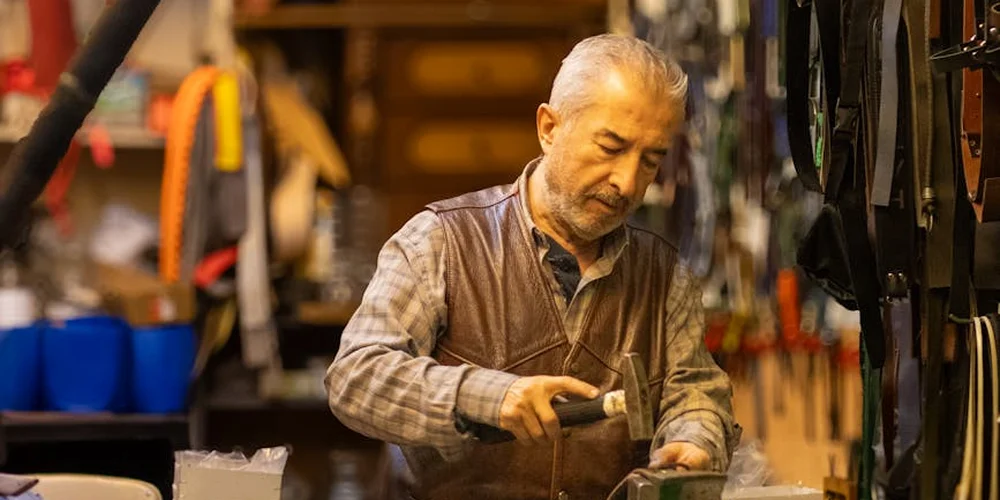 An artisan in a leather workshop applies a leather conditioner to a leather item.