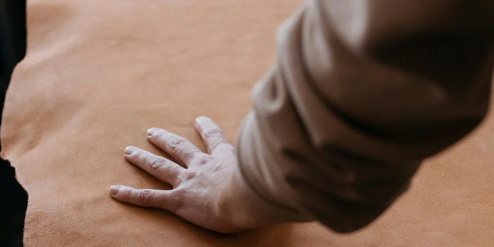 Close-up of a hand pressing a brown leather surface, illustrating a care ritual for durable leather furniture.