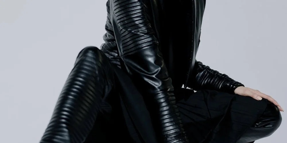 A person wearing a black leather jacket and pants, highlighting the glossy texture of leather.