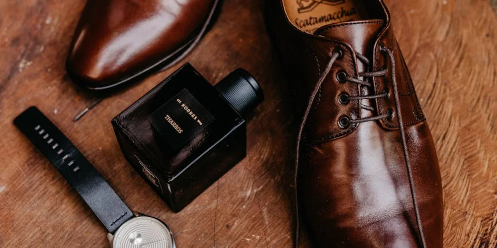 Close-up of brown leather boots and accessories laid out on a wooden surface.