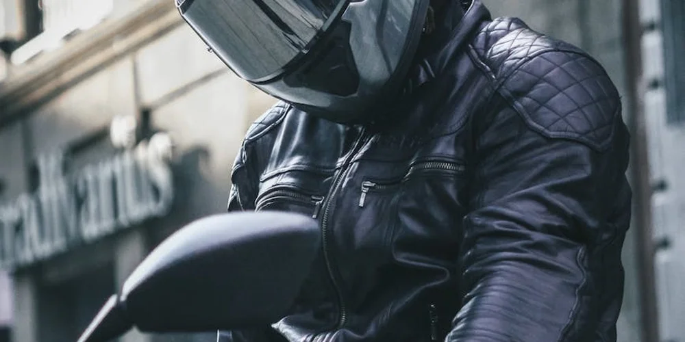 Person wearing a black leather motorcycle jacket with quilted shoulders and a full-face helmet.