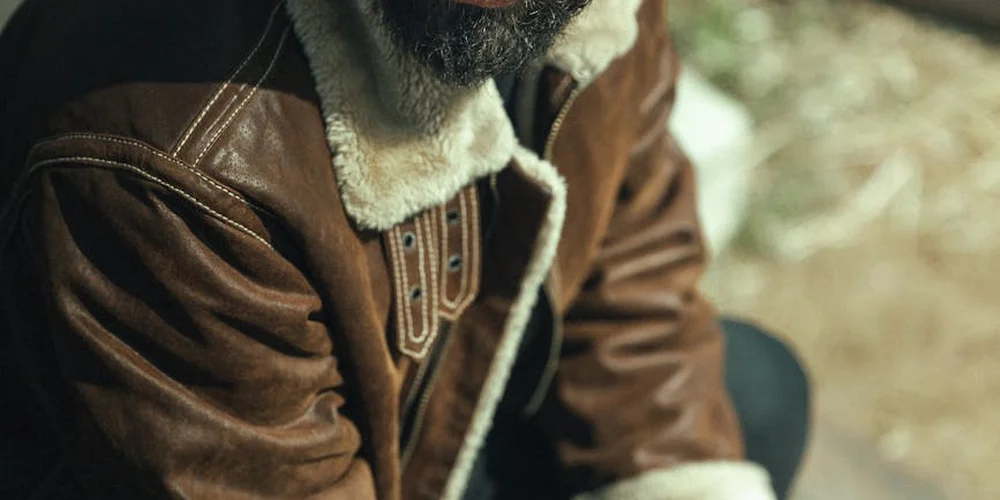 Close-up of a brown leather jacket with a shearling collar, showing the leather texture.