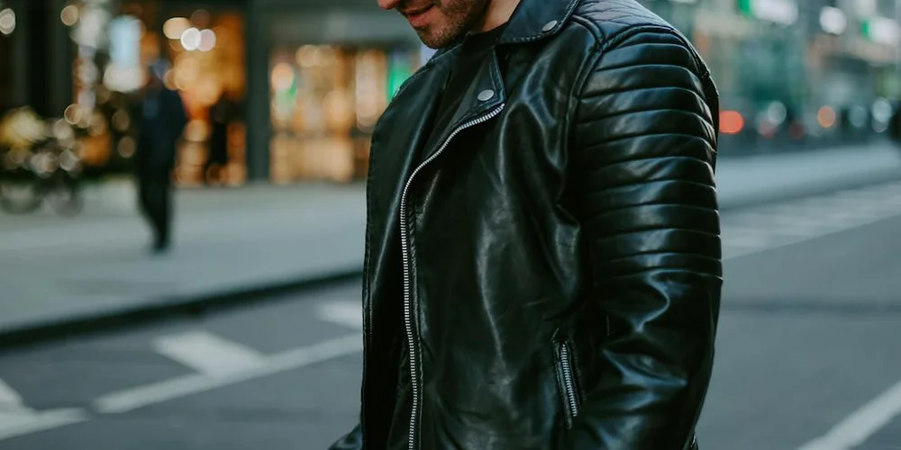 A person wearing a black leather jacket on a city street.