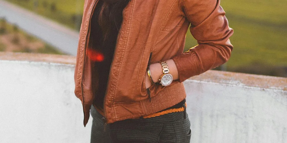 Person wearing a brown leather jacket standing outdoors near a low wall