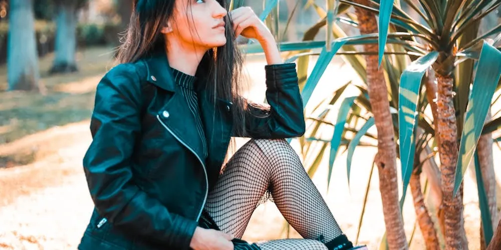 Person wearing a black leather jacket outdoors with plants in the background.