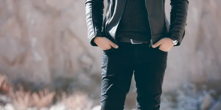 Person wearing a black leather jacket and dark pants standing with hands in pockets outdoors