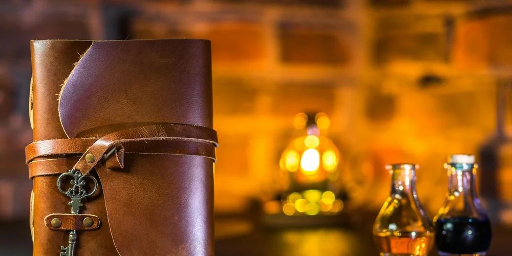 Close-up of a brown leather journal with straps on a wooden surface, with a warm, amber-lit background and blurred bottles in the distance.