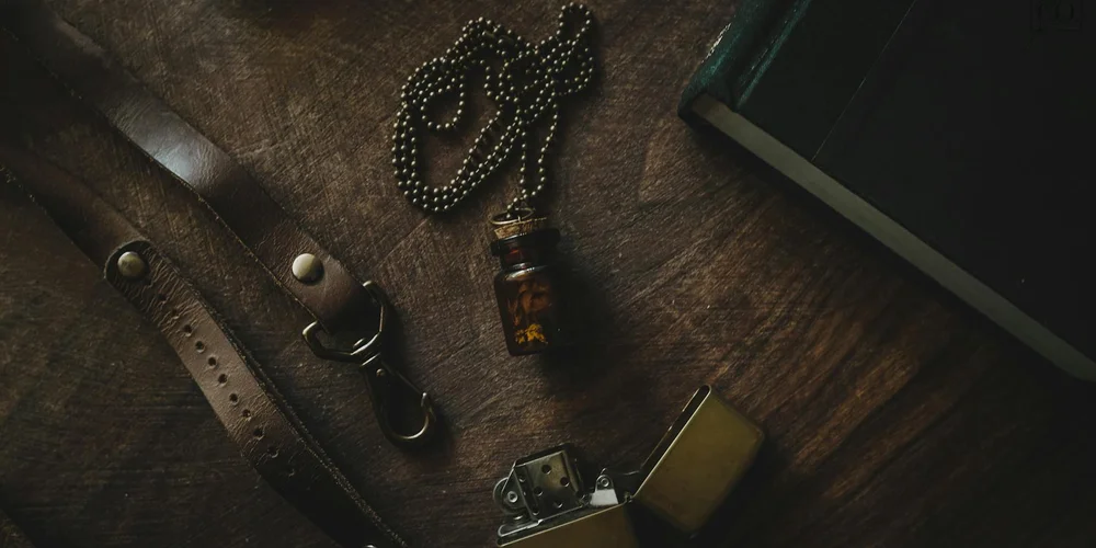 Close-up of leather care items on a dark wooden surface, including straps, a small bottle, a chain, and a lighter, suggesting tools for conditioning leather.