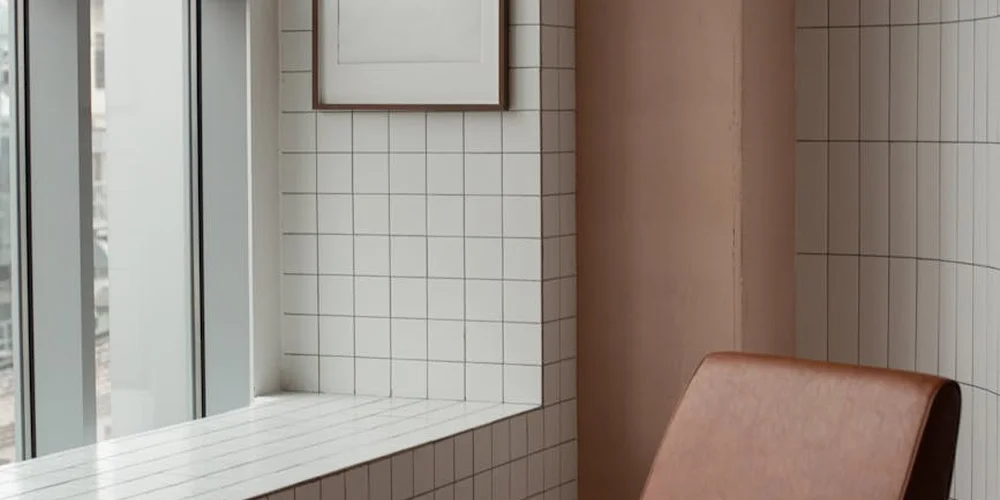 Minimal, sunlit interior with white tiled wall, window, and a brown leather seat, illustrating leather in real-world use.