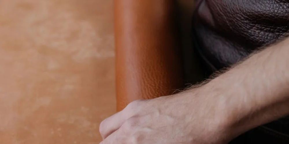 Close-up of brown leather with a light-skinned hand resting on it, highlighting texture and porosity.