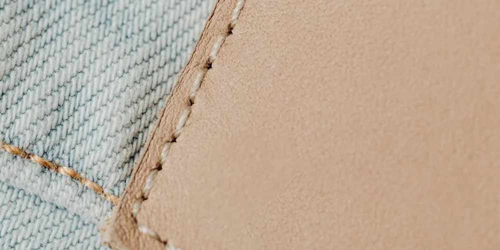 Close-up of beige leather with visible stitching next to denim fabric, illustrating careful, non-damaging printing considerations on leather surfaces.