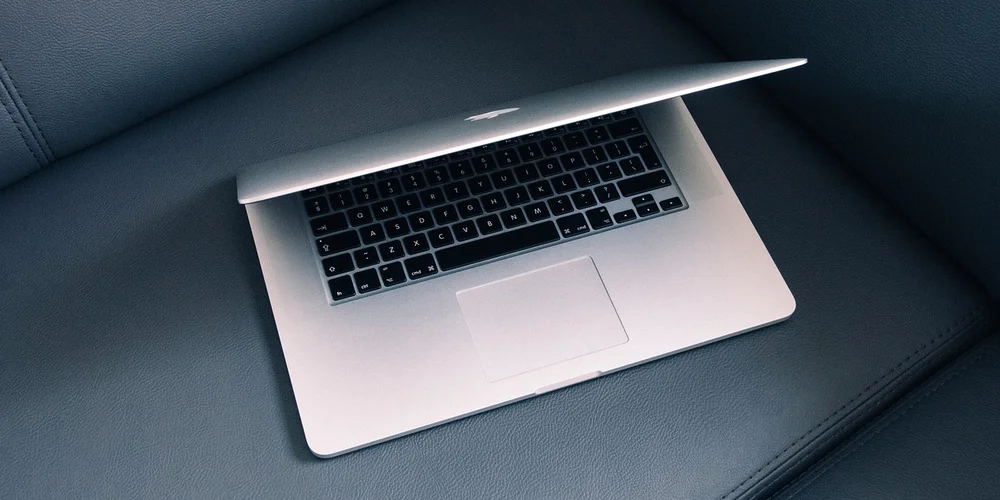 Silver laptop resting on a blue leather couch.