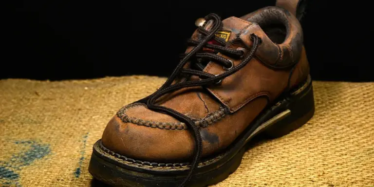 Brown leather shoe with visible stitching on a woven surface.