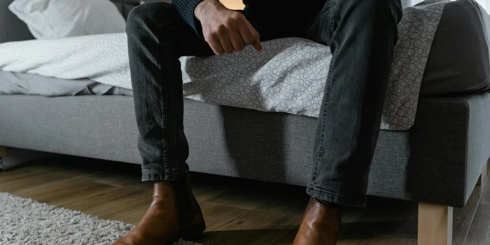 Person seated on a sofa wearing brown leather boots, highlighting common leather footwear prone to scratches and scuffs.