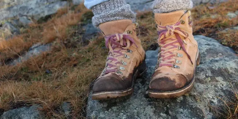 Pair of brown leather hiking boots with pink laces resting on a rocky, mossy surface