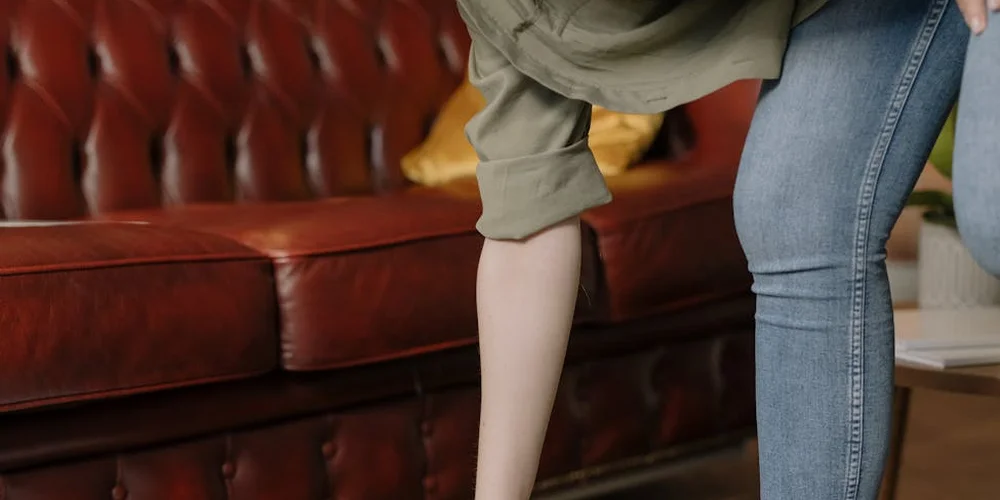 Person in a green sleeve treating a spill on a red leather sofa, focusing on the armrest area.