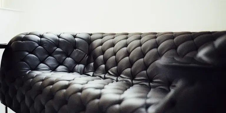 Close-up of a black tufted leather sofa with diamond-pattern upholstery