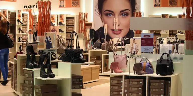 Retail display of leather handbags and boots in a store, with a large advertising poster featuring a woman's face in the background