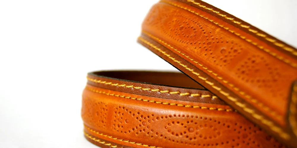 Close-up of an orange-brown leather strap with decorative perforations and white stitching.