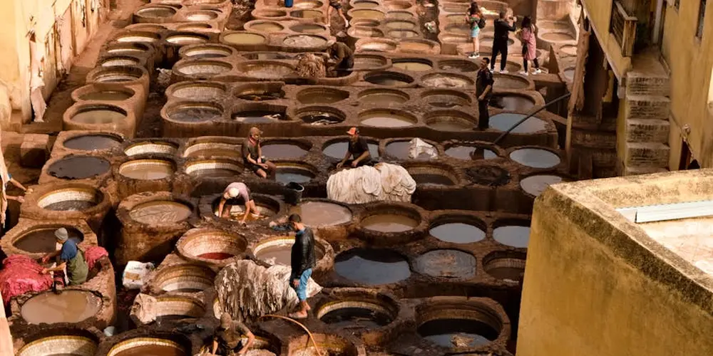 An open-air tannery with many circular leather tanning pits and workers processing hides, illustrating traditional waterproofing methods.