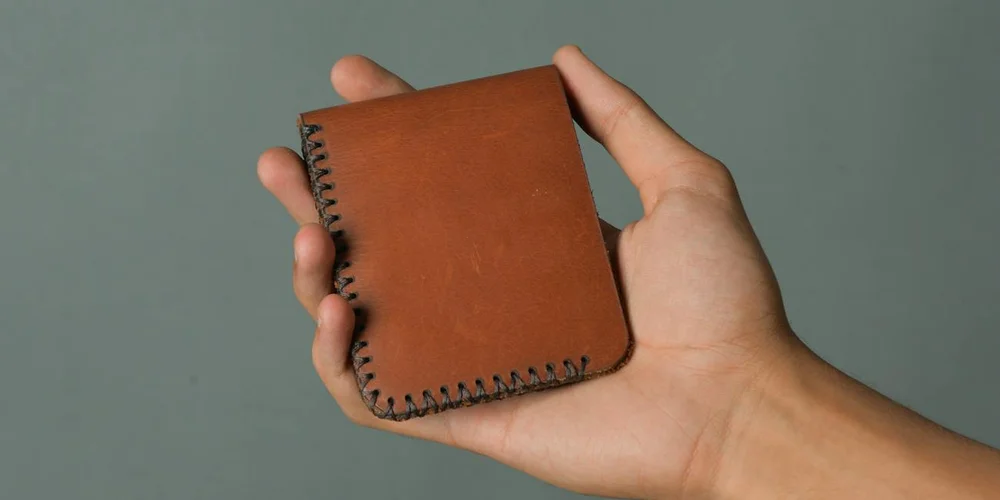 Close-up of a hand holding a small brown leather wallet with visible stitching.