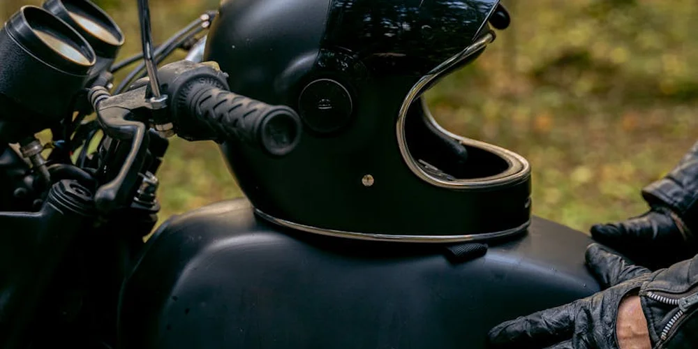 Close-up of black leather motorcycle helmet and glove resting on a bike, illustrating leather gear that benefits from conditioning and proper storage after cleaning.
