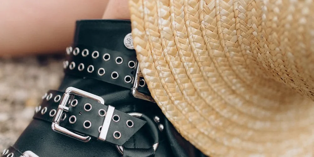 Close-up of a black leather belt with metal buckles and studs beside a woven straw hat.
