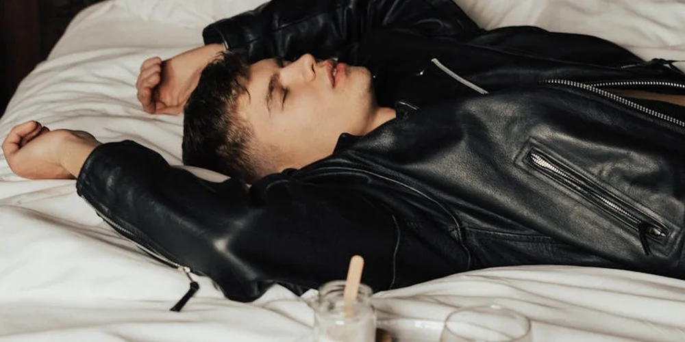 Person wearing a black leather jacket lying on a white bed