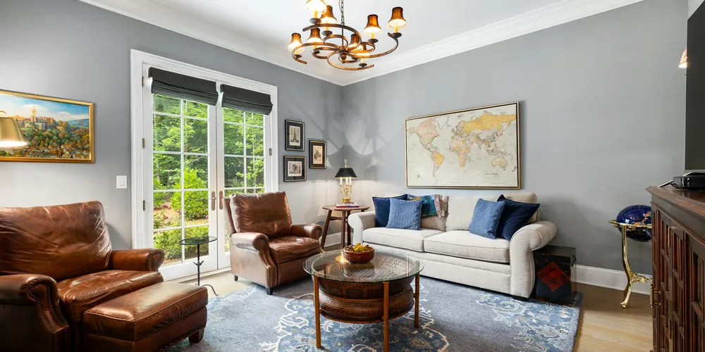 A cozy living room featuring brown leather armchairs, a light beige sofa, a wooden coffee table, a world map on the wall, and a glass door leading to a patio.