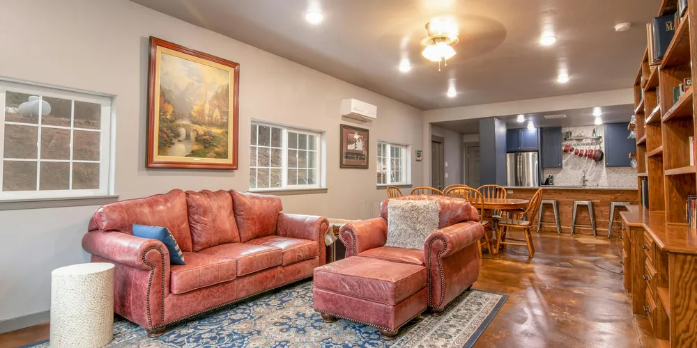 Red leather sofa with matching ottoman in a spacious living room featuring wood floors, a painting on the wall, and built-in shelves.
