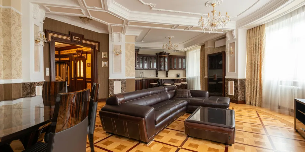 Luxurious living room with dark brown leather sofas, glass coffee table, and large windows letting in natural light.