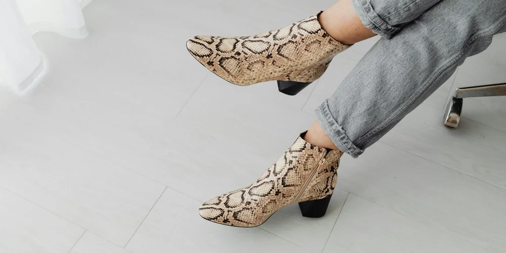 Close-up of snakeskin-patterned ankle boots on a person seated with legs crossed, ready for mink oil treatment
