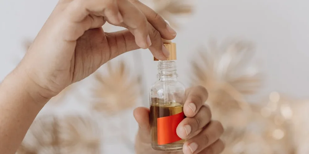 Close-up of hands using a dropper to dispense mink oil from a small glass bottle with an amber liquid for leather care.