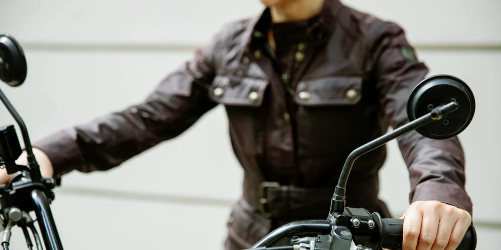 Rider wearing a brown leather jacket grips motorcycle handlebars.