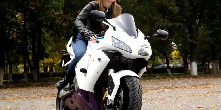 Rider wearing a black leather jacket on a white motorcycle in a park.