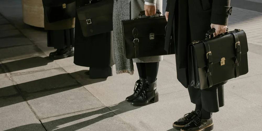 People in dark coats carrying leather briefcases and bags on a city sidewalk