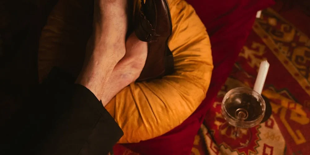 A close-up of a hand grasping a wet leather shoe, ready to start the drying process, with a patterned textile and a glass visible in the background.