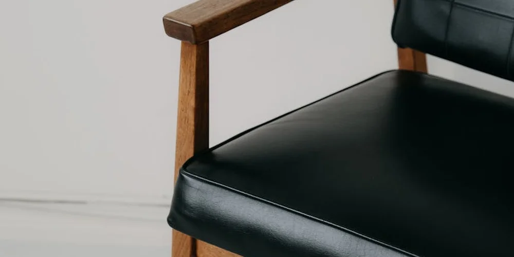 Close-up of a black leather chair seat with a wooden armrest
