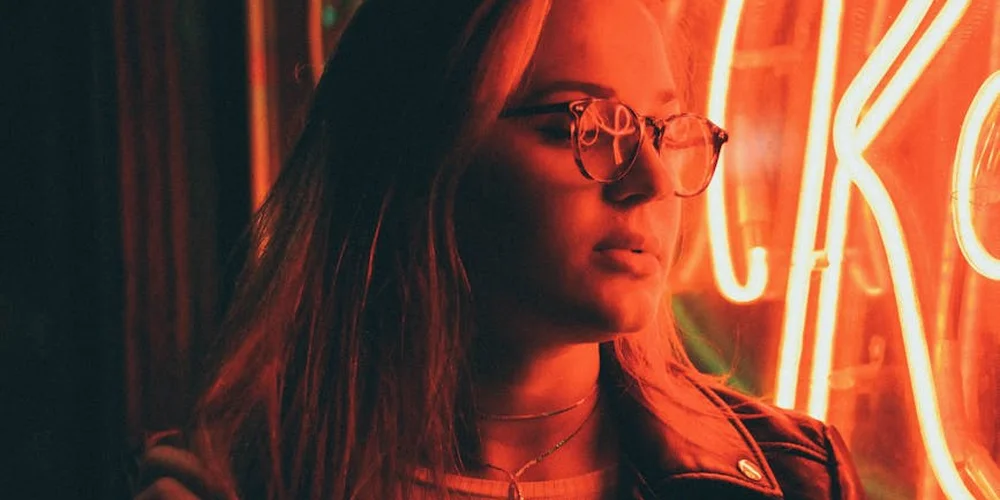 Side-profile of a person wearing a leather or faux leather jacket under red neon lights