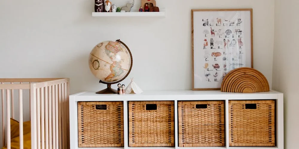 Nursery scene with a white dresser, four wicker baskets, a globe, and framed art on the wall.