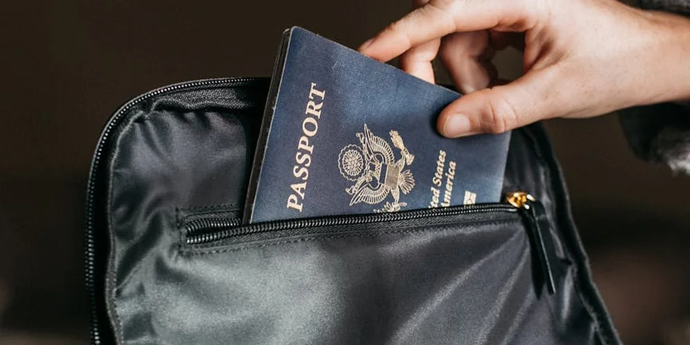Close-up of a hand placing a blue passport into the inner pocket of a black leather bag.